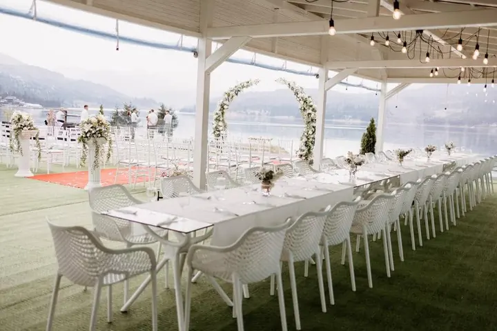 Decor de eveniment cu aranjamente florale și mese albe pe terasa cu vedere spre lac