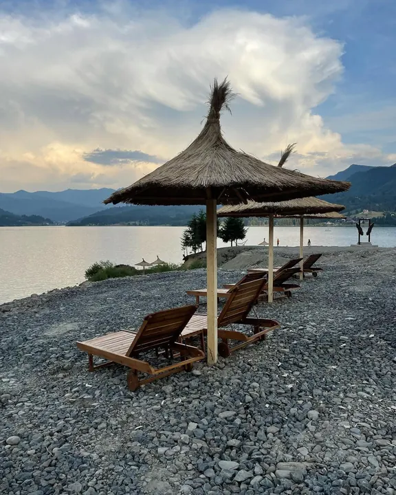 Șezlonguri de lemn sub umbrele din stuf, lângă lacul Colibița